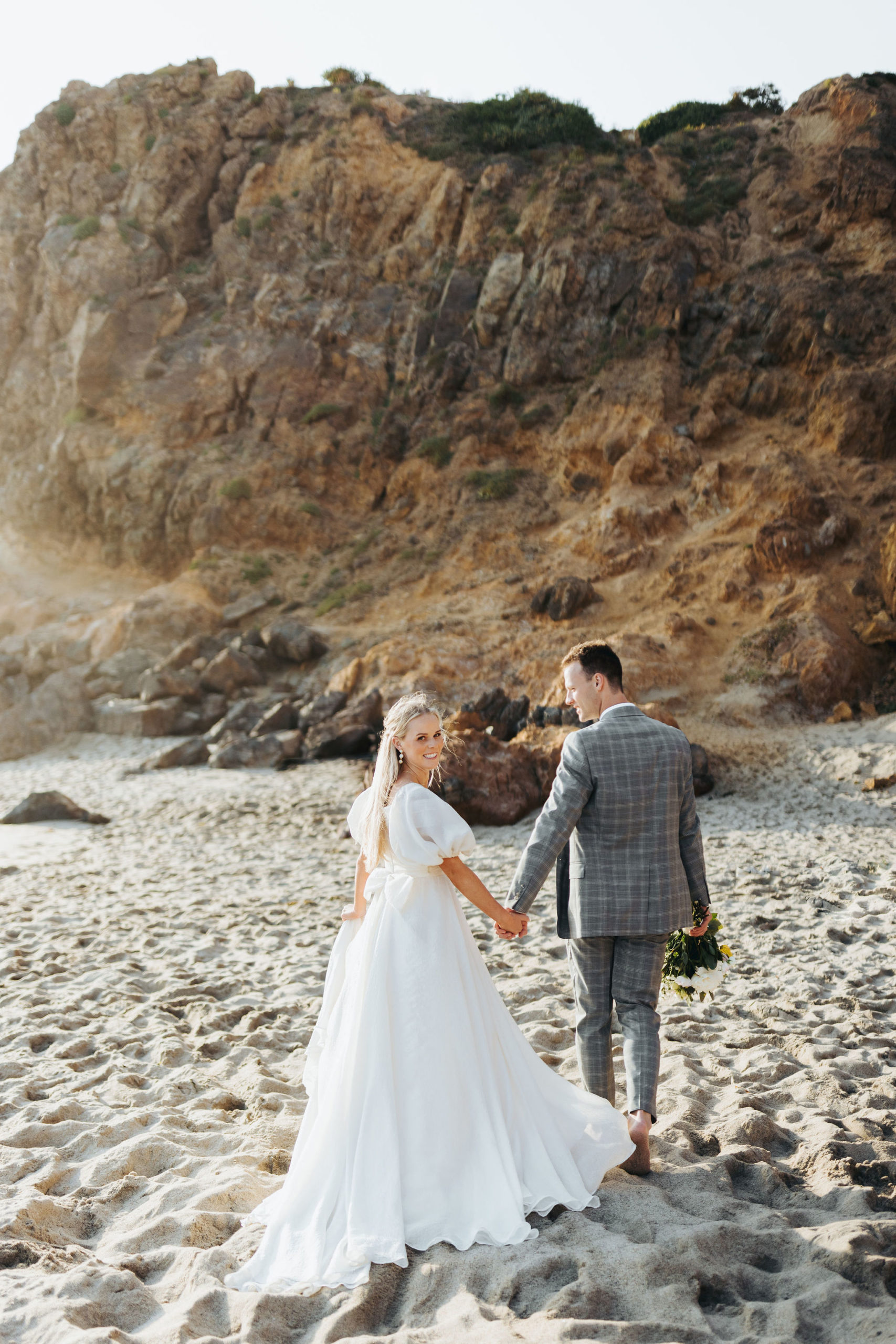 bride and groom holding hands walking on a beach