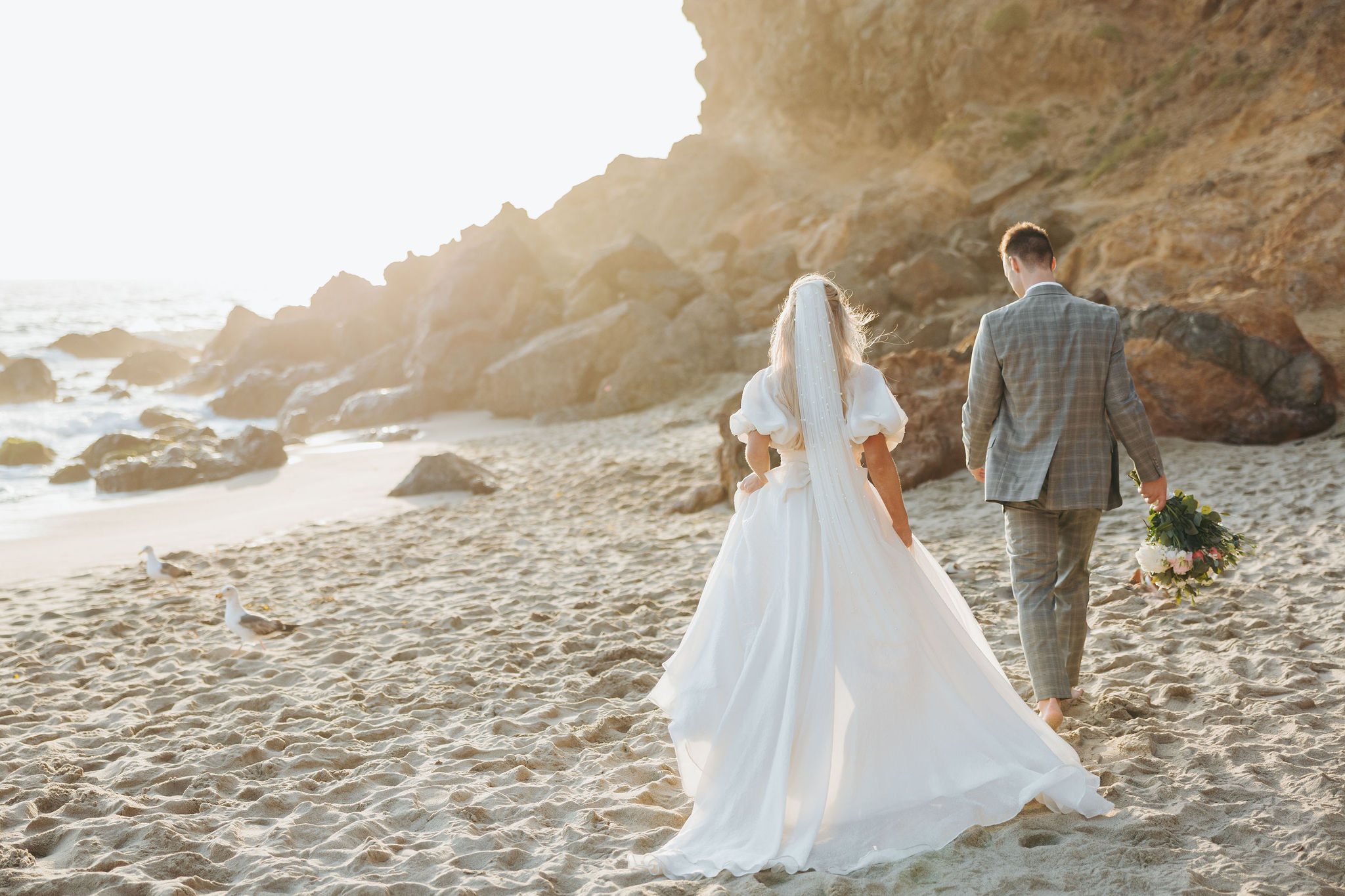 bride and groom holding hands walking on a beach