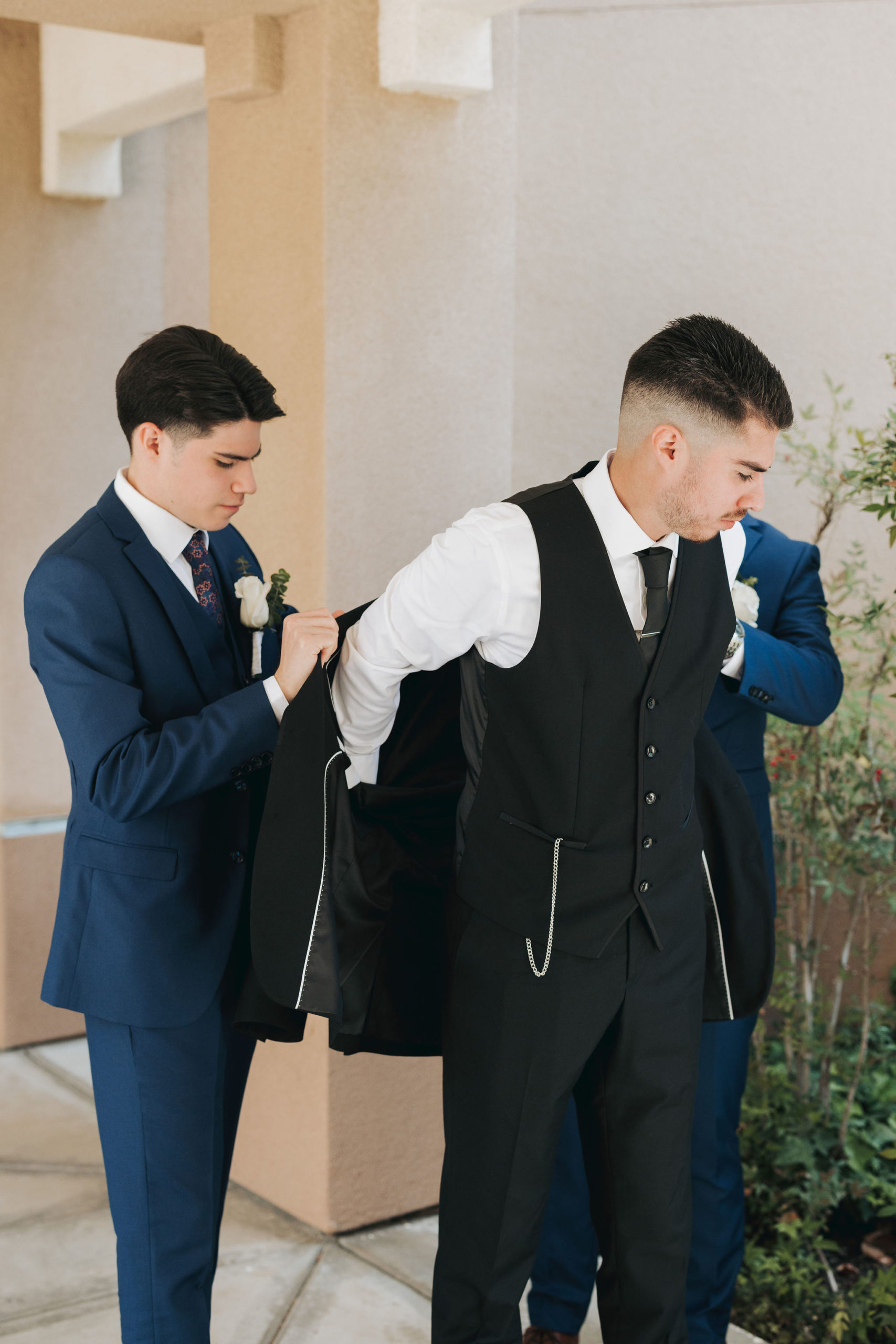 groomsmen helping groom put on coat before wedding ceremony in temecula california