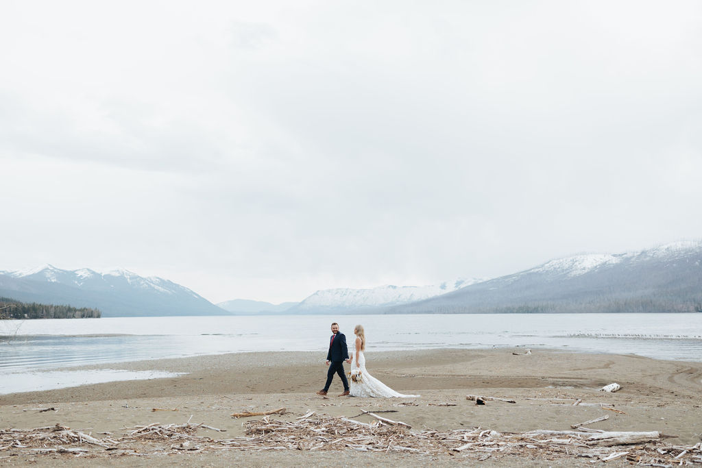 bride and groom walking on glacier national park lake with mountains in the background