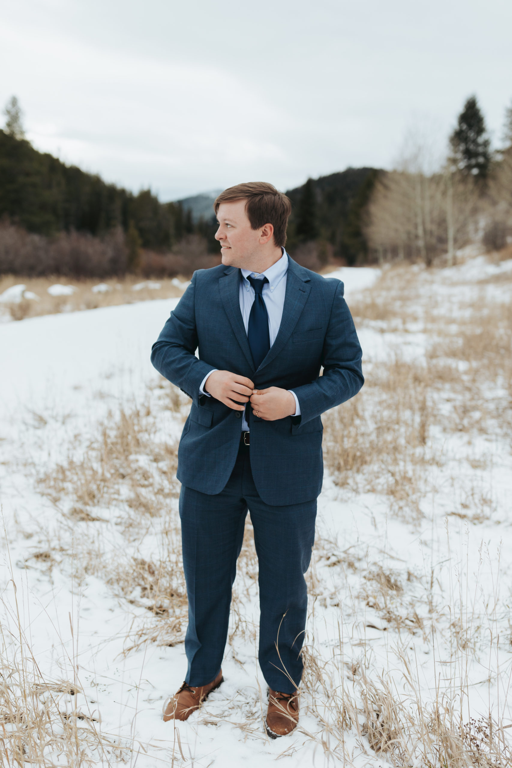 groom in blue suit in snow and mountains after elopement ceremony in grand teton national park 