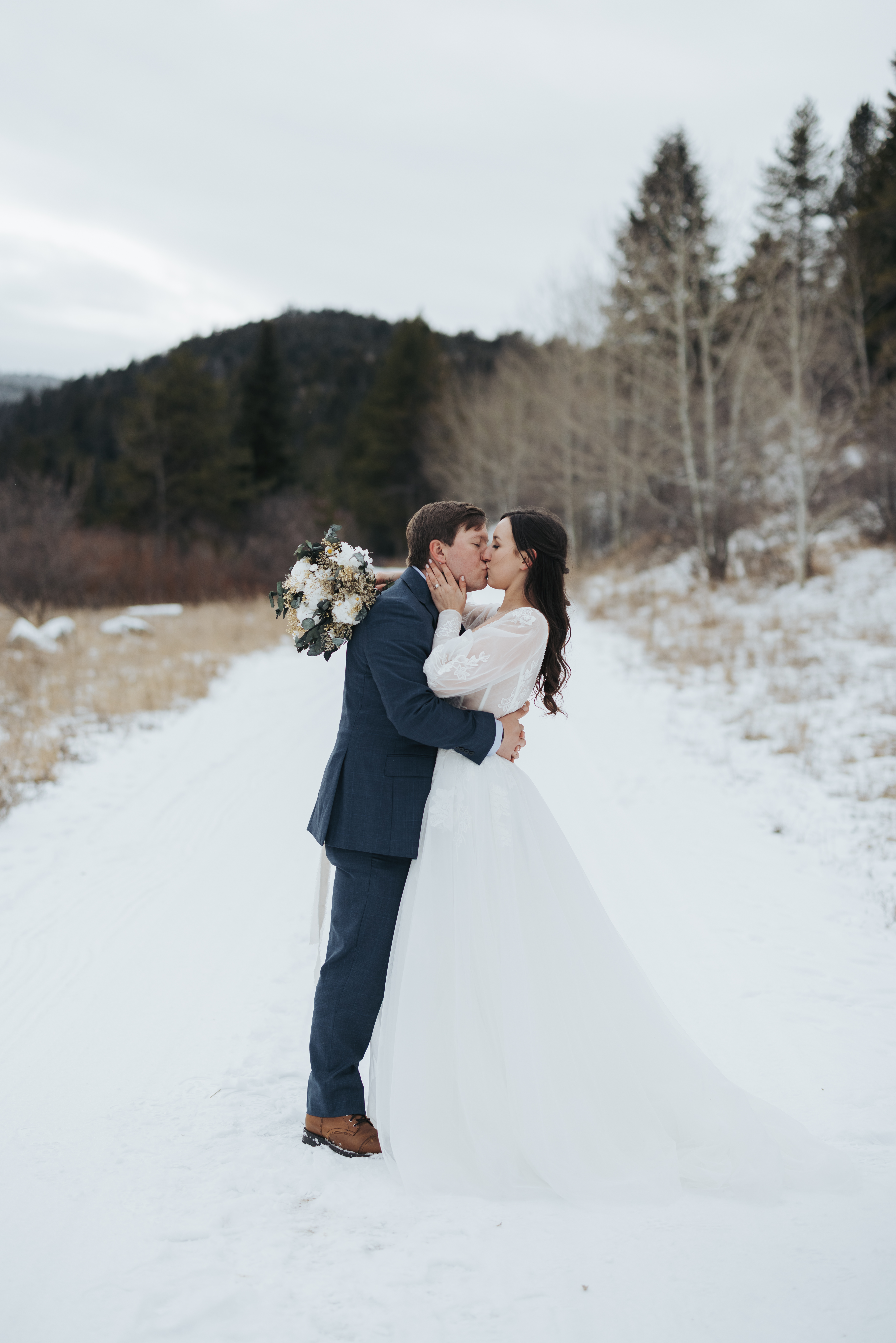 bride and groom kissing in snow and mountains
