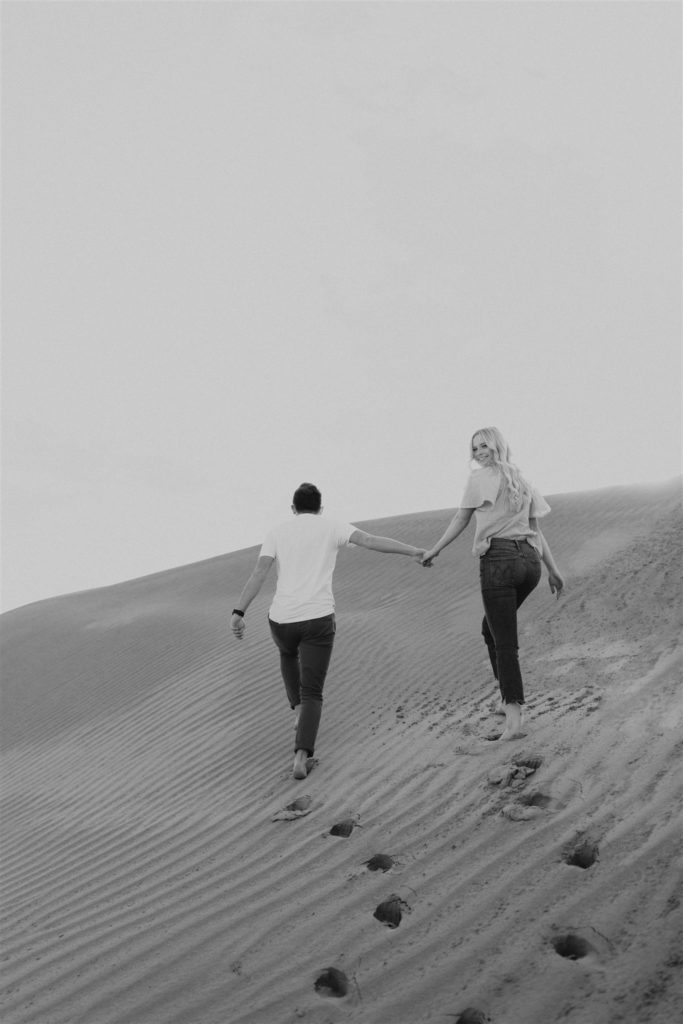 Black and white image of a Couple walking on a sand dune for their engagement session