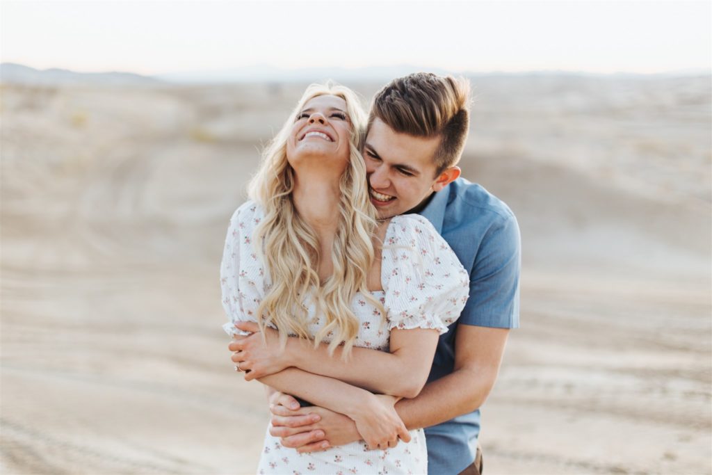 Couple hugging on sand dune in front of mountains