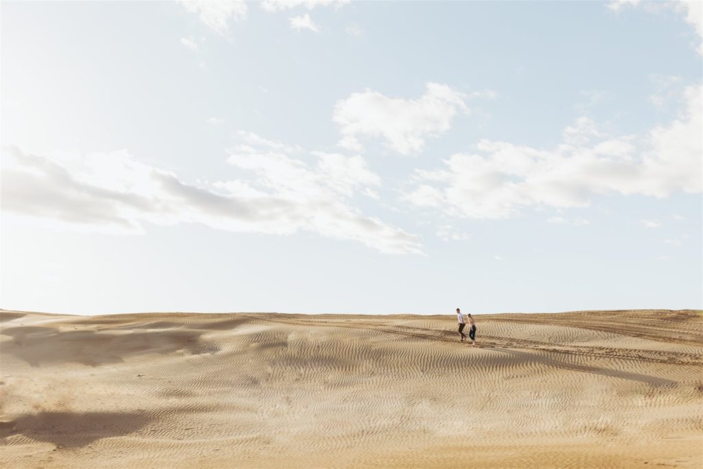 Couple walking on sand dune during their engagement session