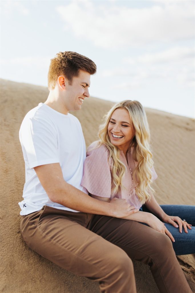 Couple laughing on the sand dune during their engagement session