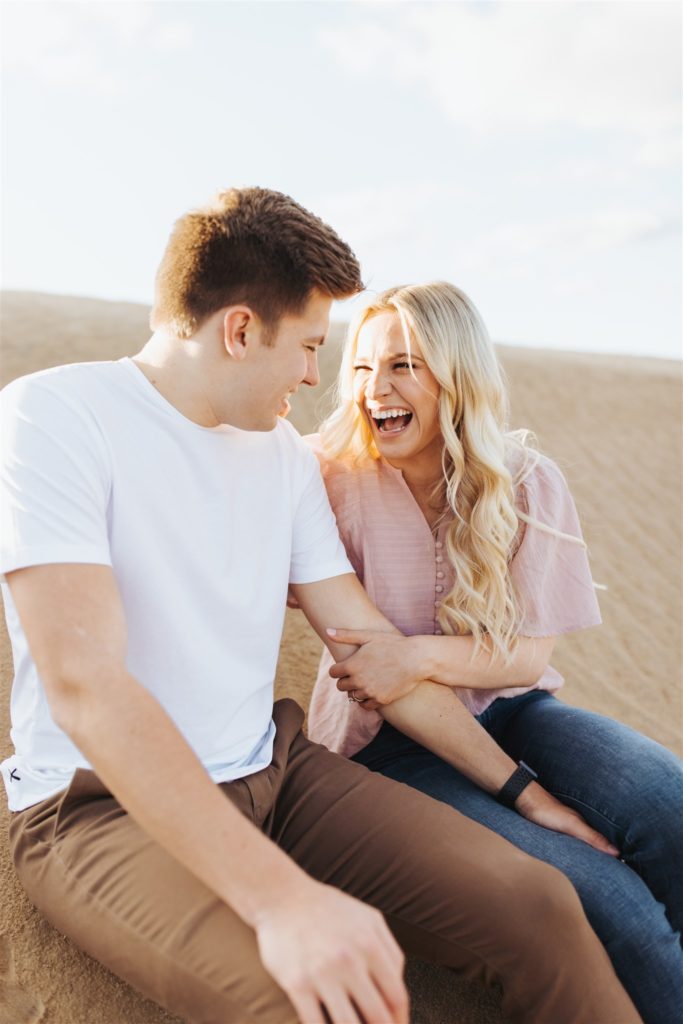 Couple laughing on the sand dune during their engagement session