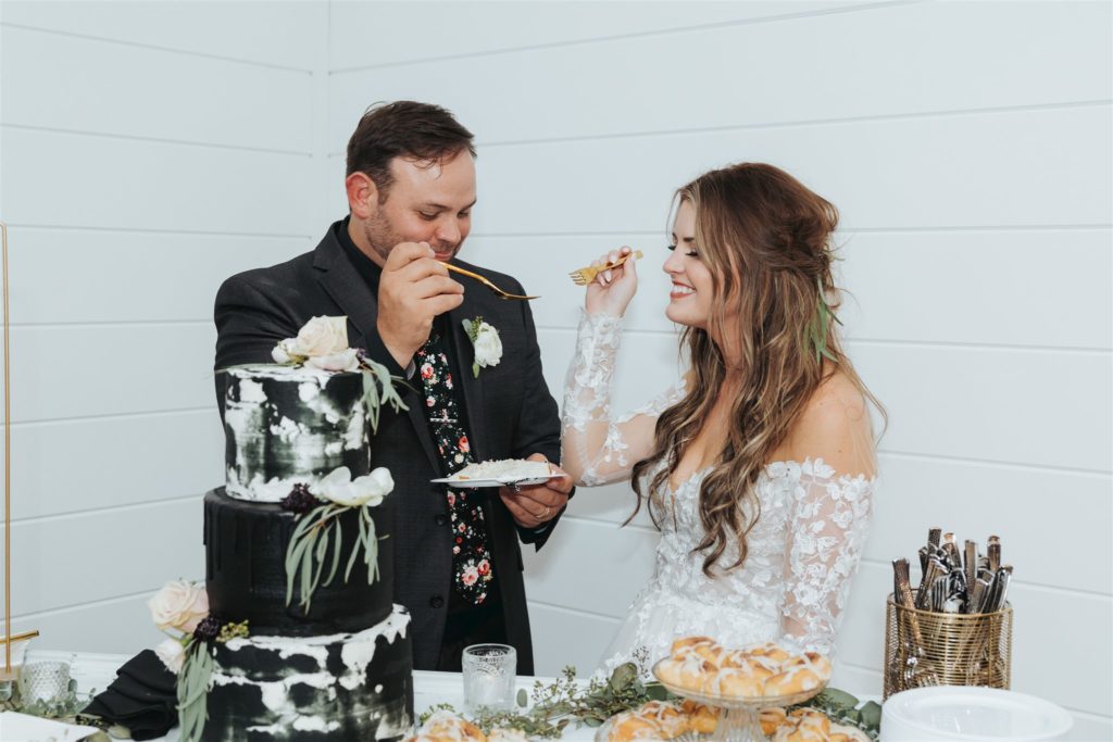 bride and groom eating white and black wedding cake with florals