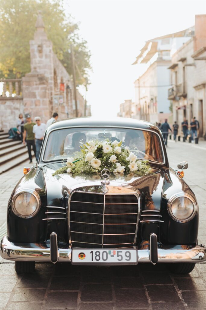 bride and groom exit car with flowers on the hood