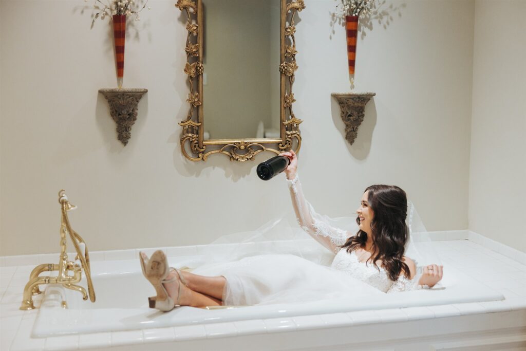 bride getting ready sitting on bathtub with champagne