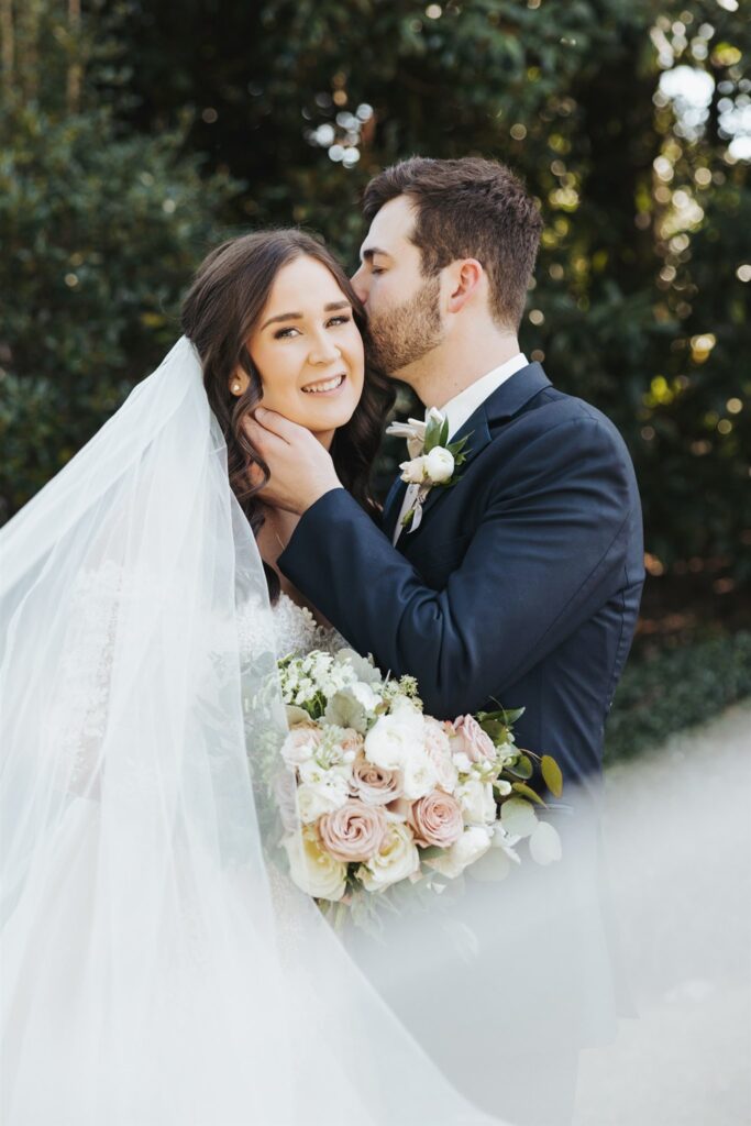 bride and groom hugging in the garden with wedding veil in front