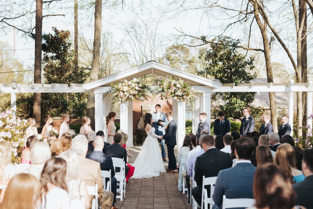 wedding ceremony outdoors with white chairs and floral arch