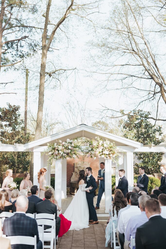 wedding ceremony outdoors with white chairs and floral arch