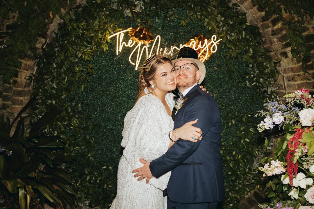 Bride and groom hugging in front of neon sign