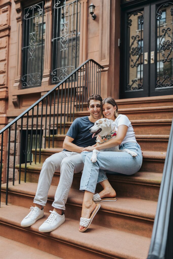 man and woman holding dog on stairs in front of building in new york city