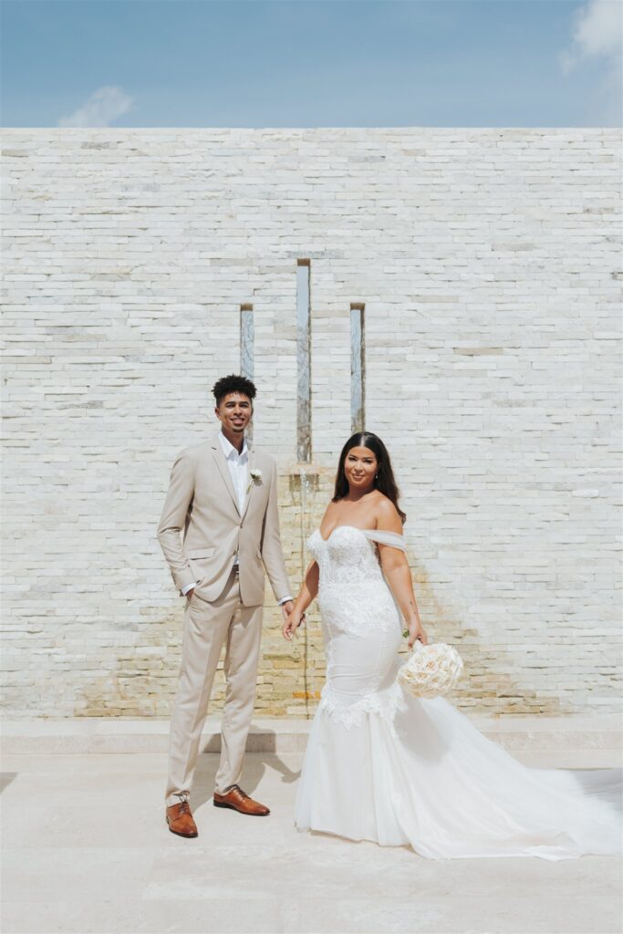 bride and groom in front of a tan brick wall