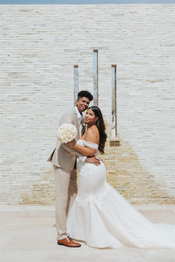 bride and groom in front of a tan brick wall