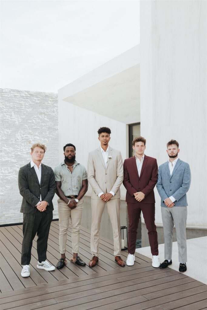 groom and groomsmen posing in front of white wall