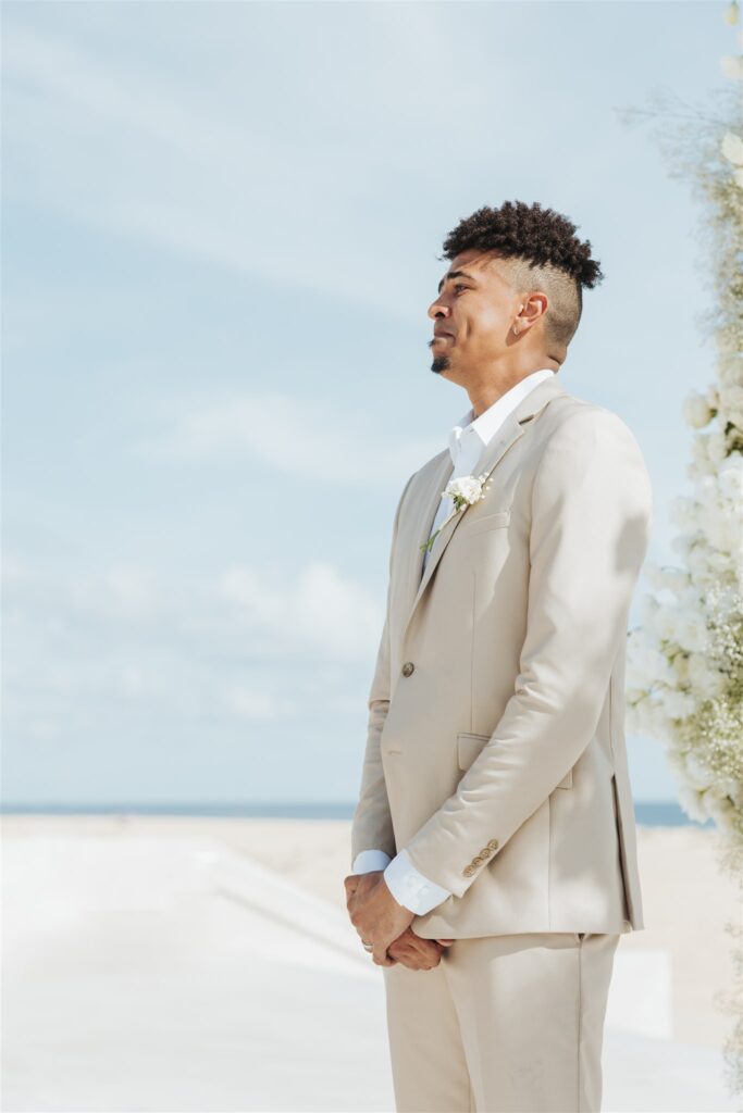 groom in tan and white suit on the beach