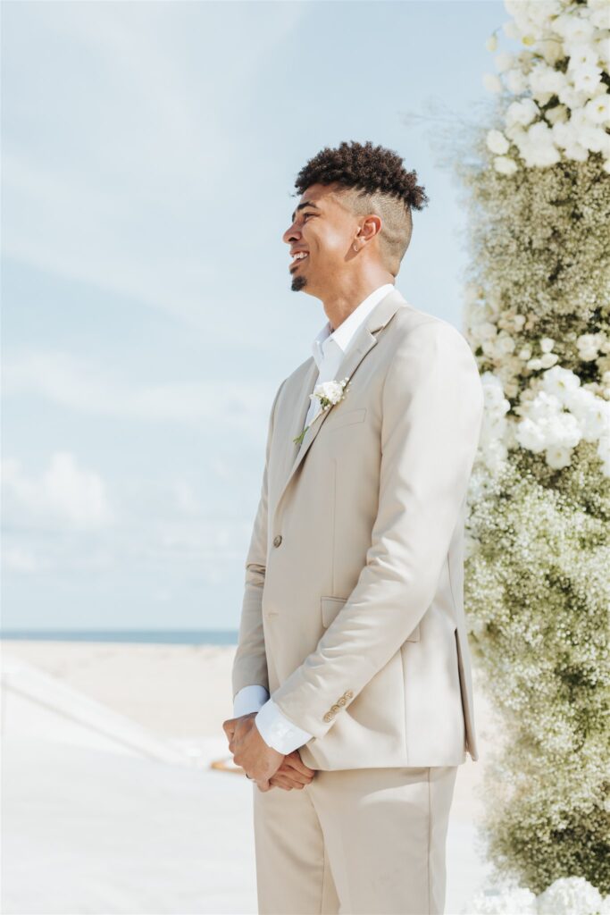 groom in tan and white suit on the beach
