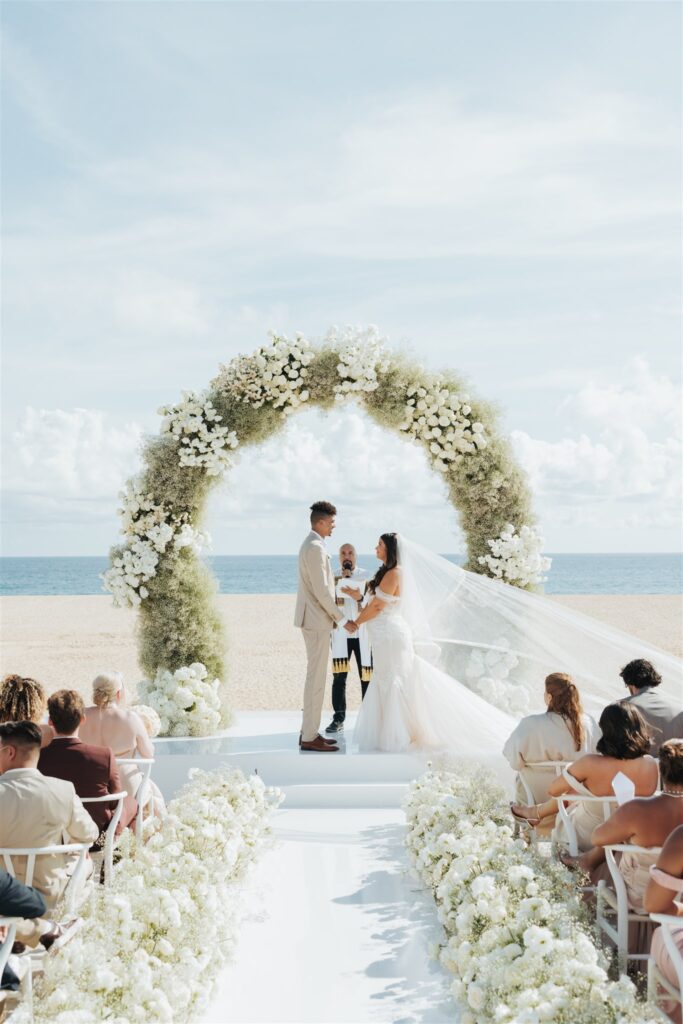 bride and groom wedding ceremony with floral arch at the beach in los cabos