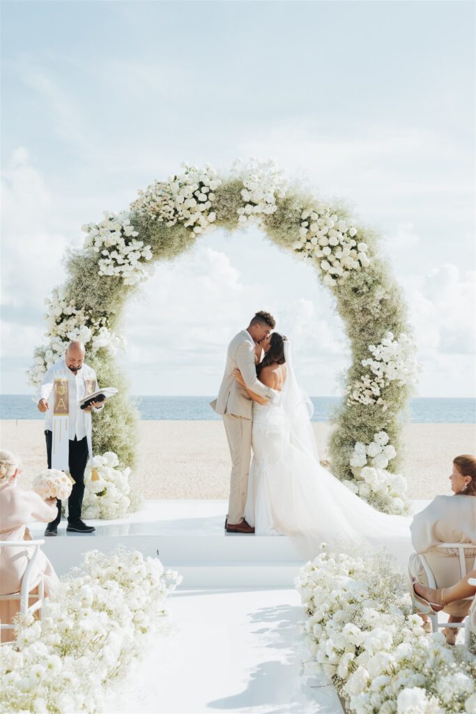 bride and groom wedding ceremony with floral arch at the beach