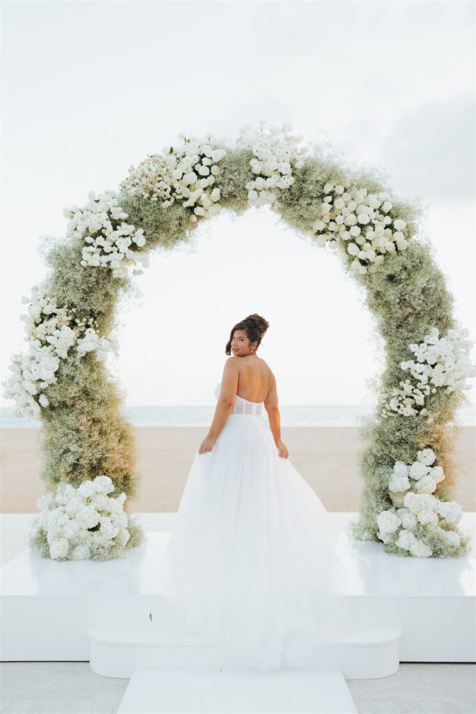 bride under floral arch at the beach