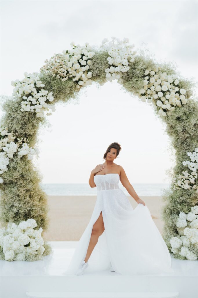 bride under floral arch at the beach