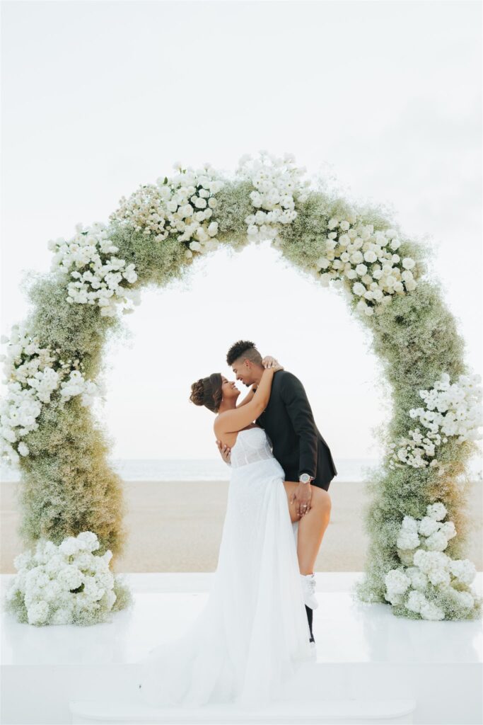 bride and groom under floral arch at the beach nobu hotel los cabos