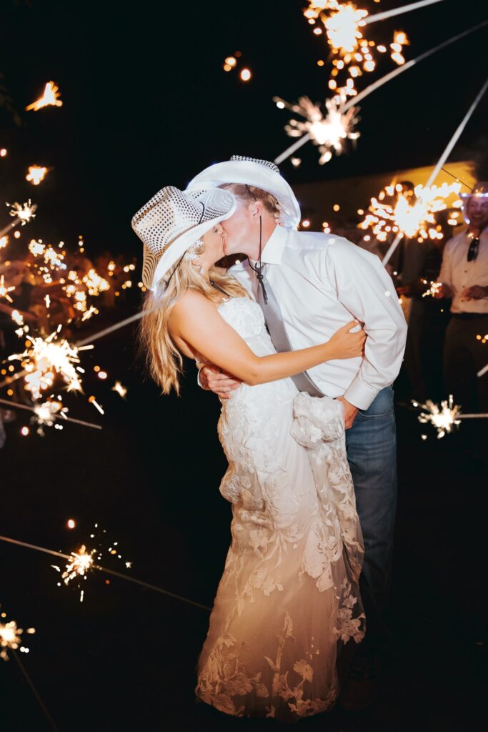 bride and groom kissing with cowboy hats and sparklers