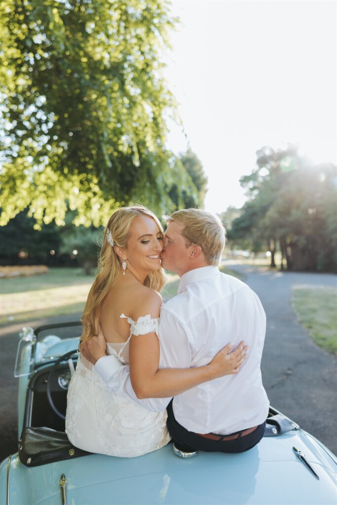 bride and groom kissing in front of bright blue, antique getaway car