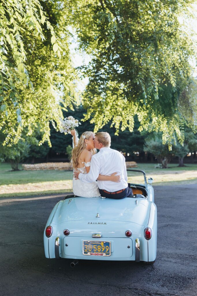 bride and groom kissing in front of bright blue, antique getaway car