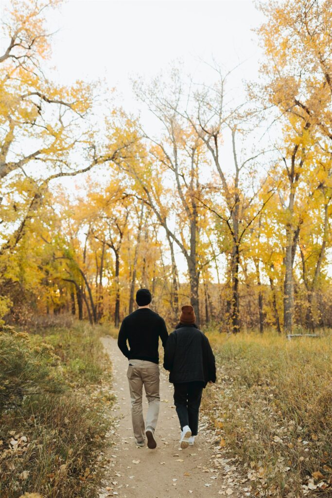 couple holding hands and walking in the woods in the fall