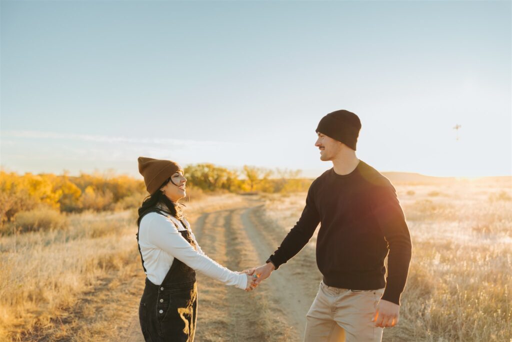 couple holding hands and walking in a field in the fall